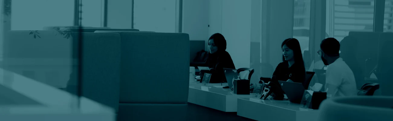 Teal-tinted photo of a modern office with people working at a front desk or call center, used as a banner for the contact us page.