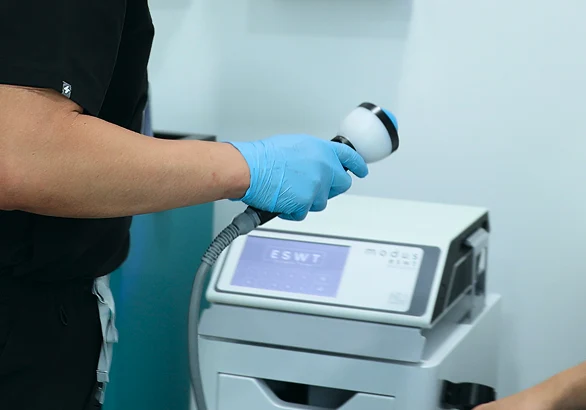 Gloved technician using an ESWT machine handpiece demonstrating treatment procedure.