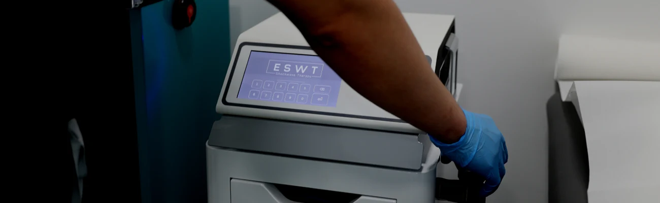 Gloved hand operating an Extracorporeal Shockwave Therapy machine in a clinical setting