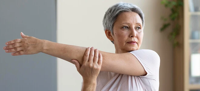 Senior woman with short gray hair stretching her arm across her chest during a home exercise routine.